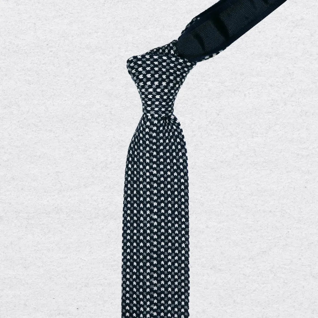 Black and white patterned knitted tie with knot on a textured background