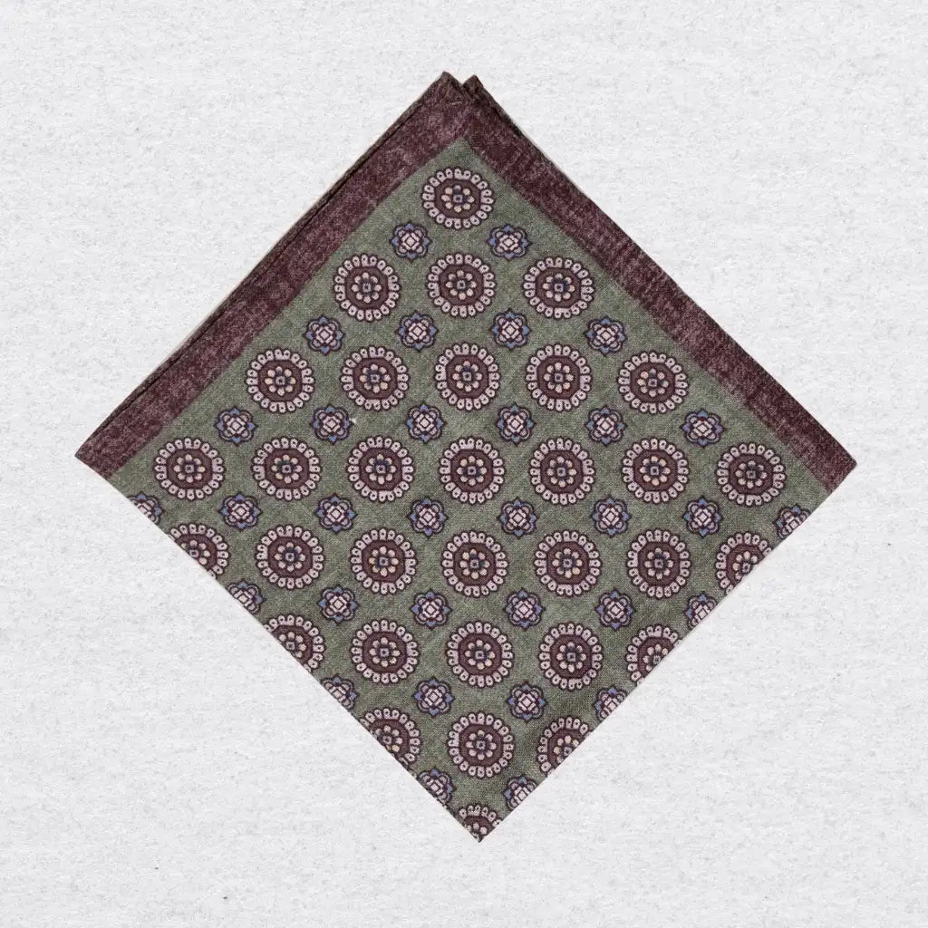Pistachio green linen pocket square with brown medallion motif folded on a grey background