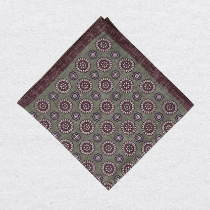 Pistachio green linen pocket square with brown medallion motif folded on a grey background