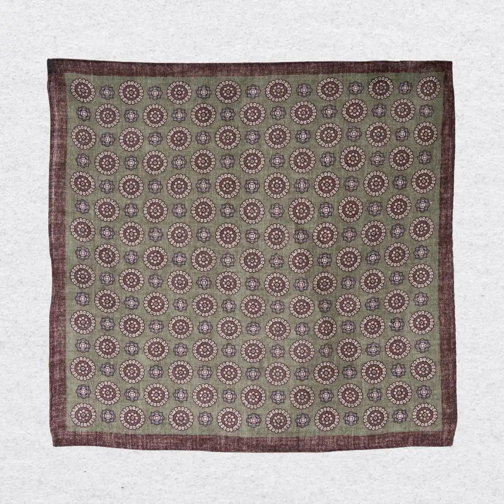 Pistachio green linen pocket square with brown medallion motif hanging against a grey background