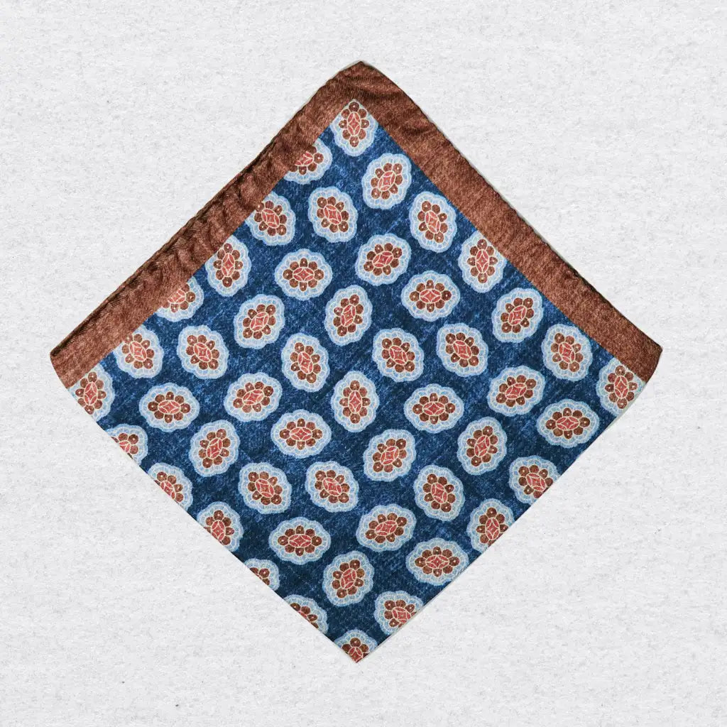 Blue silk pocket square with cinnamon border and medallions on a grey background