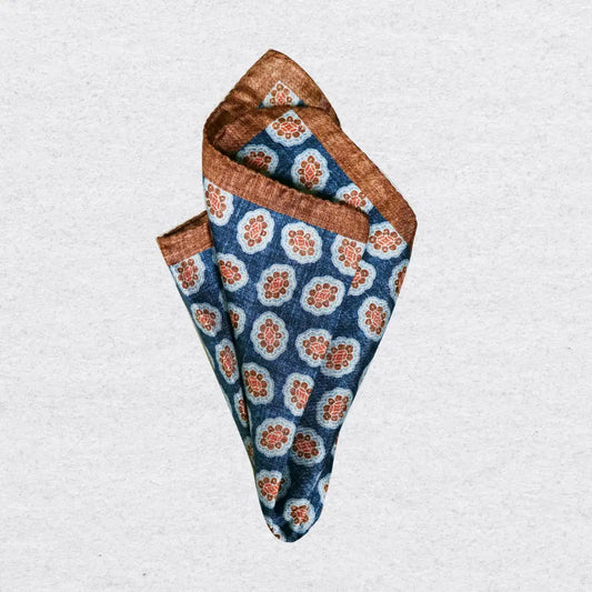 Folded silk pocket square with cinnamon coloured medallions on a light grey background