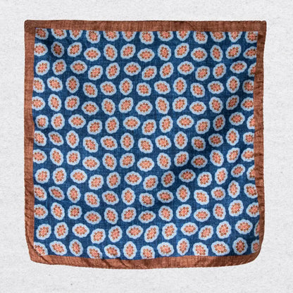 Silk pocket square with cinnamon coloured medallions and a bold border hanging against a light grey background