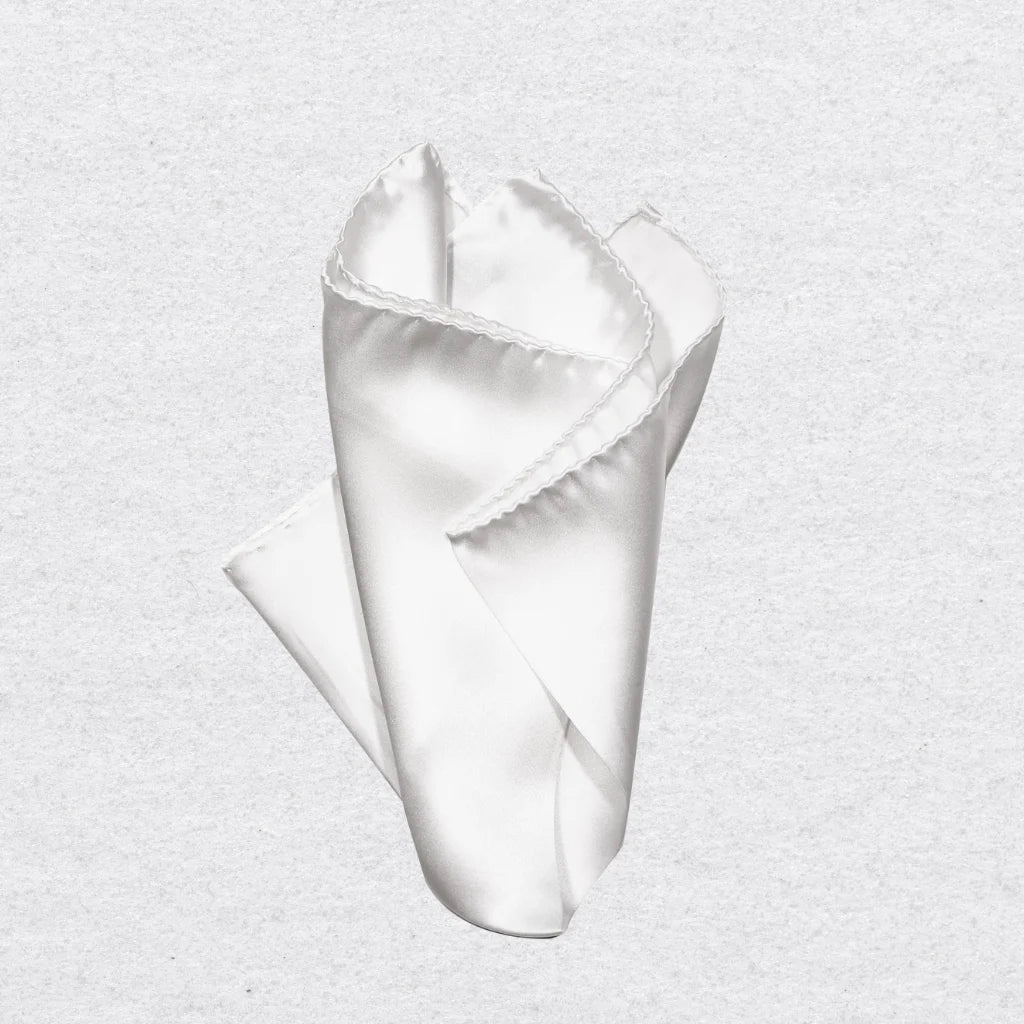 White silk pocket square pinched into a point on a grey background