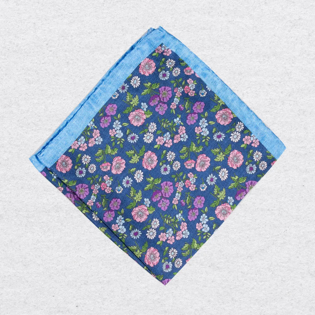 Blue silk pocket square with a pink floral pattern and light blue border on a grey background