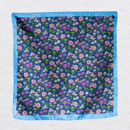 Floral patterned silk pocket square with blue border hanging against a grey background