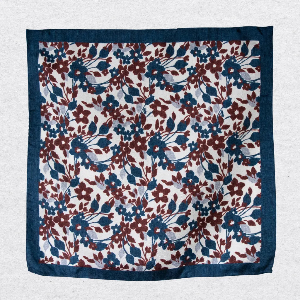 Floral patterned silk pocket square in navy and red, hanging on a textured grey background