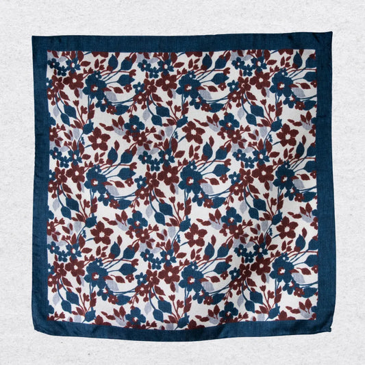 Floral patterned silk pocket square in navy and red, hanging on a textured grey background
