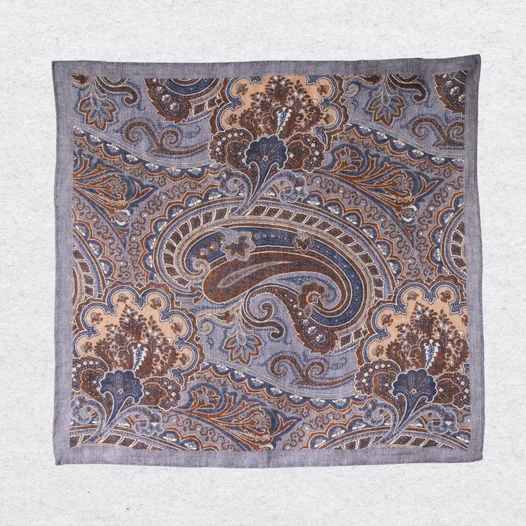 Paisley patterned linen pocket square in grey and tobacco brown hanging against a grey background