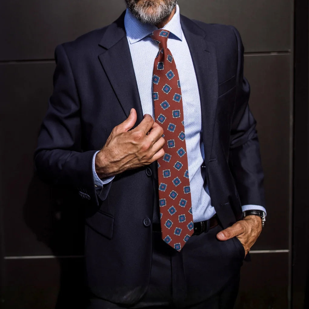 Man wearing a dark suit with a patterned tie against a neutral background