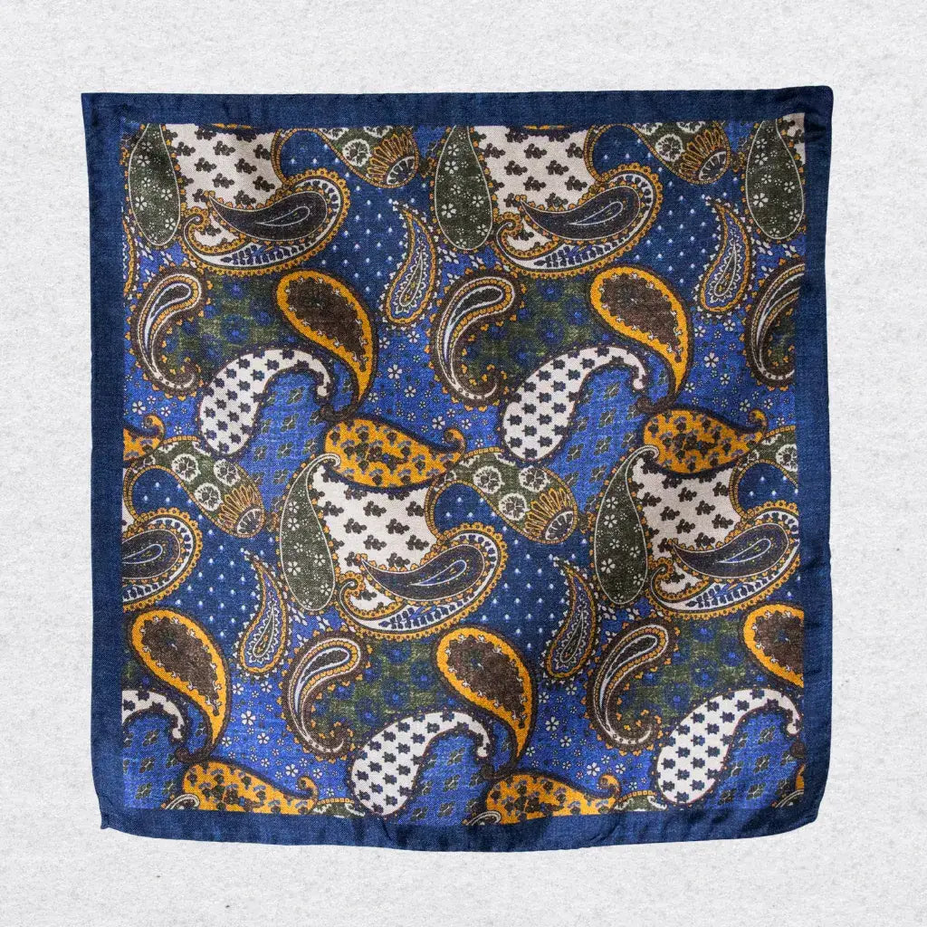 Blue and gold paisley pocket square hanging against a grey background