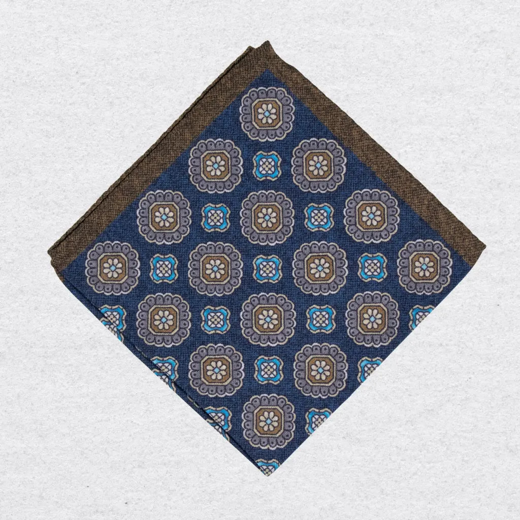 Navy blue pocket square with brown and beige floral medallion pattern on a grey background