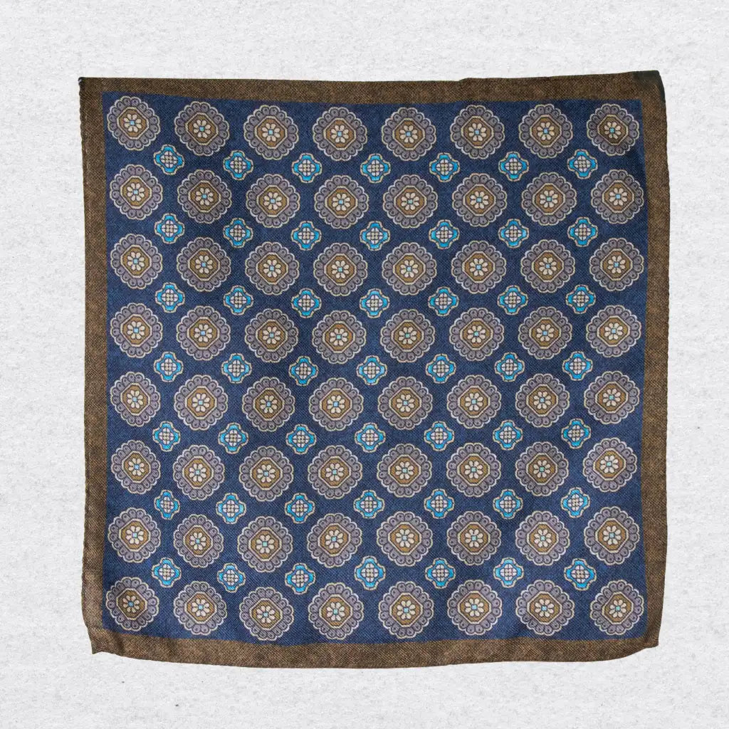 Navy blue pocket square with brown and beige floral medallion pattern hanging against a grey background