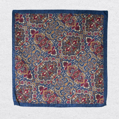 Navy and gold paisley wool-silk pocket square hanging against a light grey background