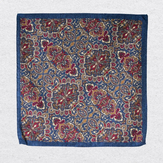 Navy and gold paisley wool-silk pocket square hanging against a light grey background