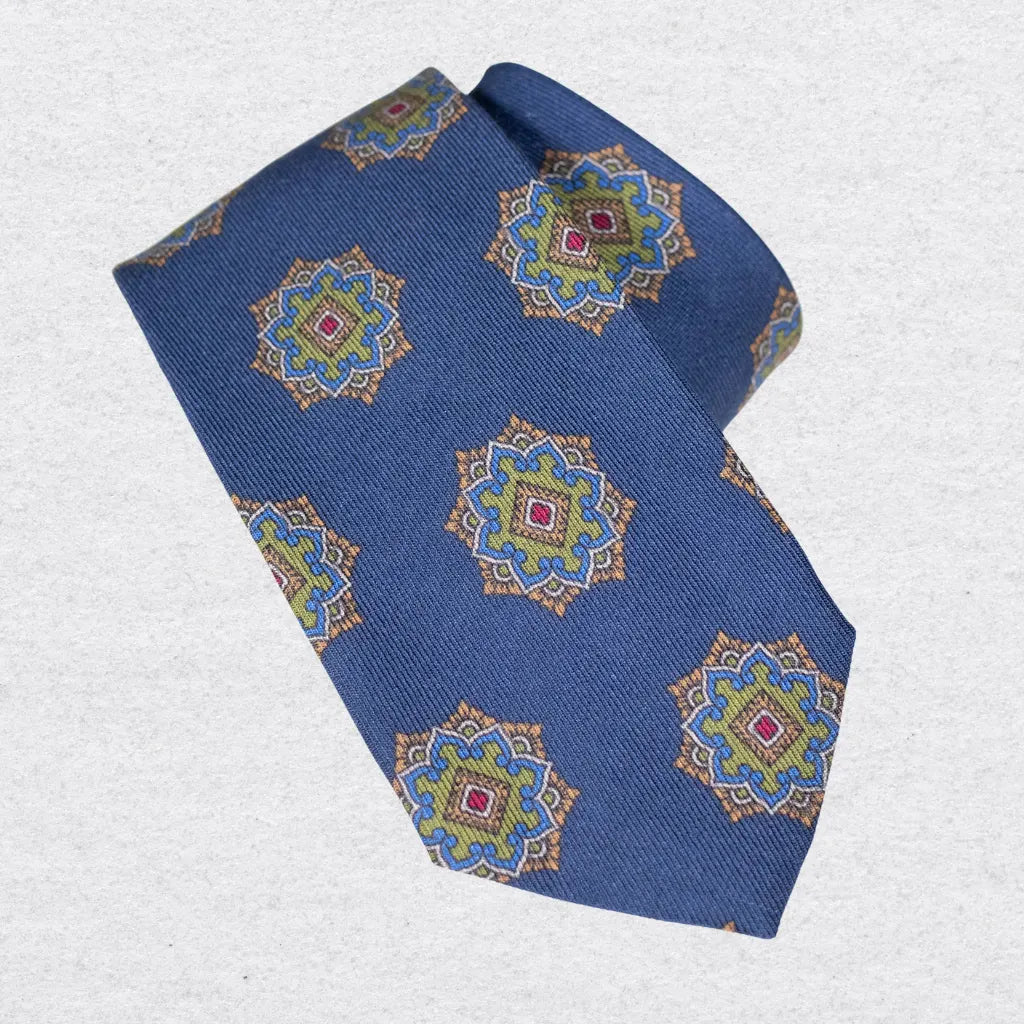 Blue wool-silk tie with a green medallion motif, rolled on a white background