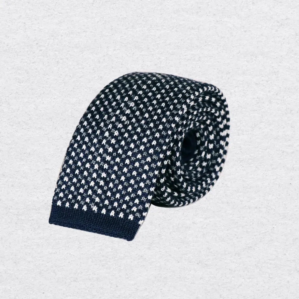 Black and white spotted knitted tie rolled on a textured background