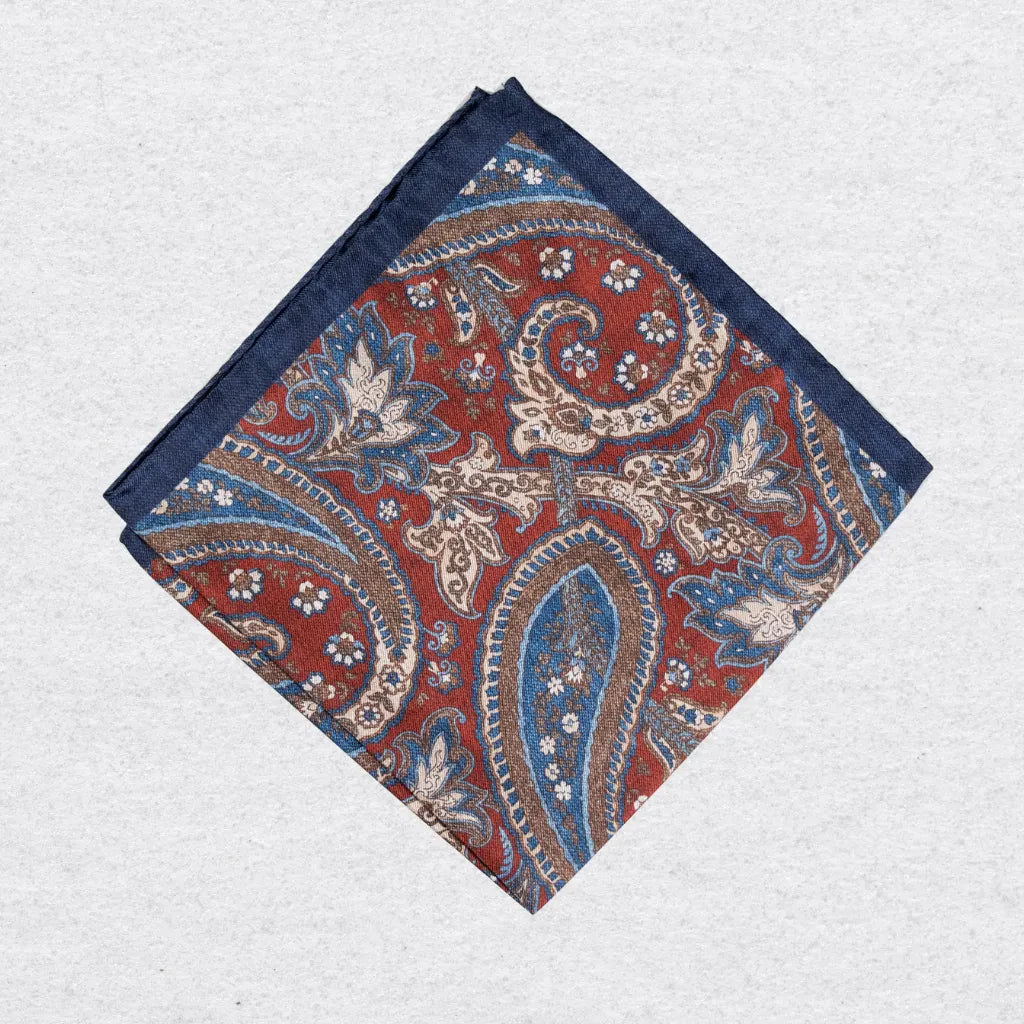 Rustic navy pocket square with a red and blue paisley pattern on a grey background