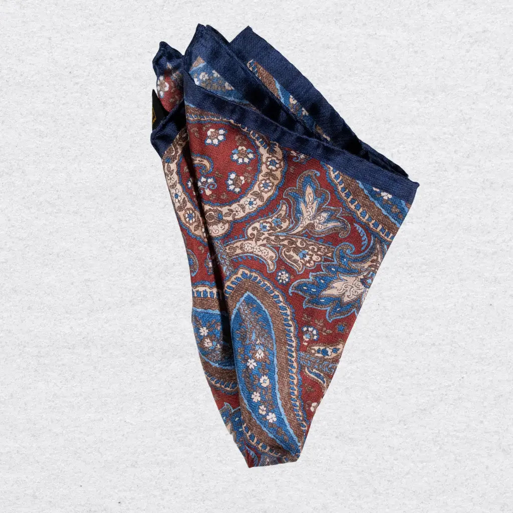 Folded red and navy paisley patterned silk pocket square on a grey background