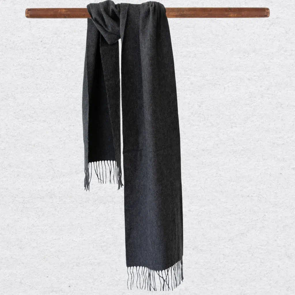 Charcoal gray scarf with tassels hanging on a wooden rod against a light gray background