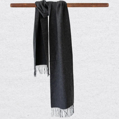 Charcoal gray scarf with tassels hanging on a wooden rod against a light gray background