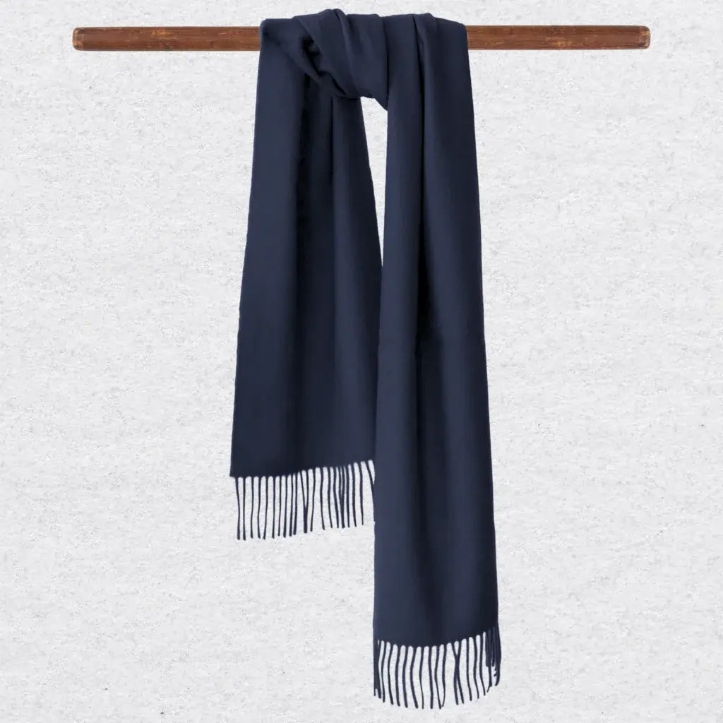 Navy blue cashmere scarf with tassels on a wooden rod against a light gray background
