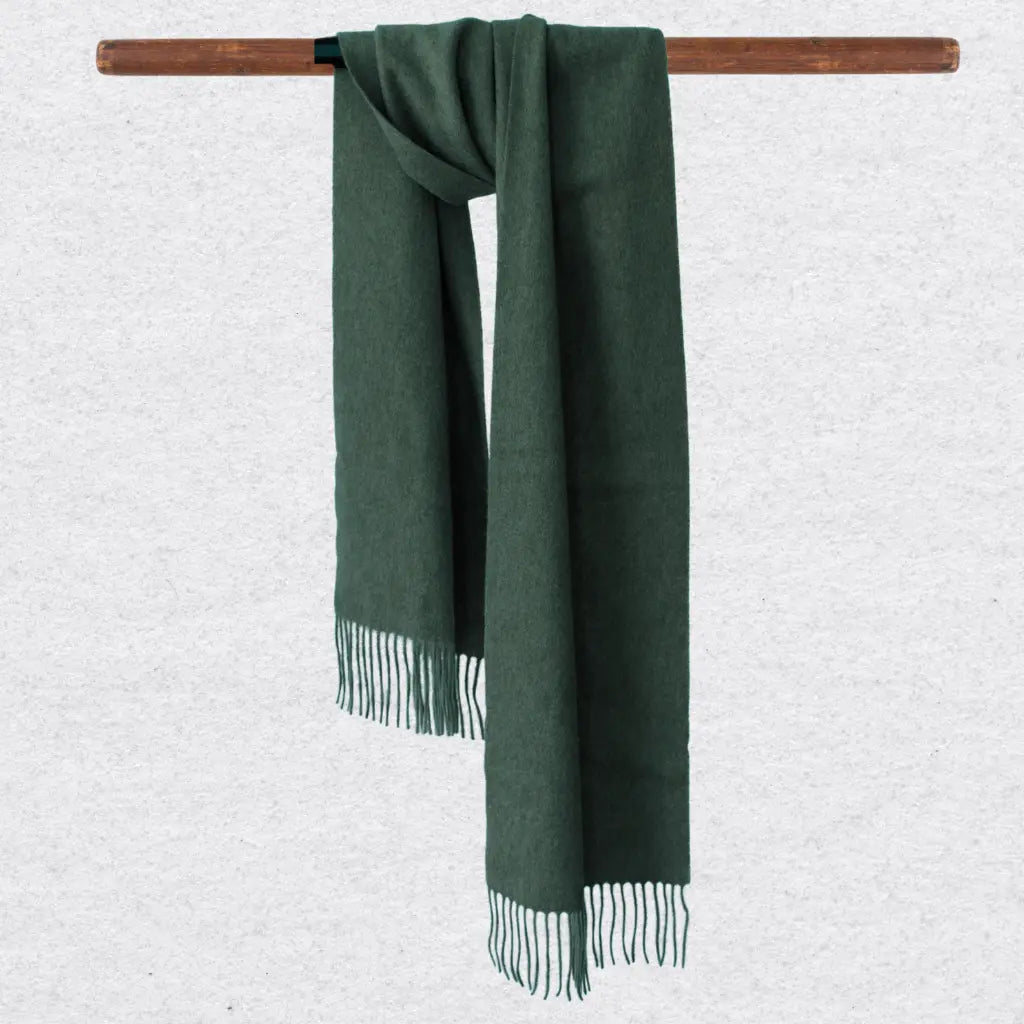 Green cashmere scarf with fringes on a wooden rod against a light gray background