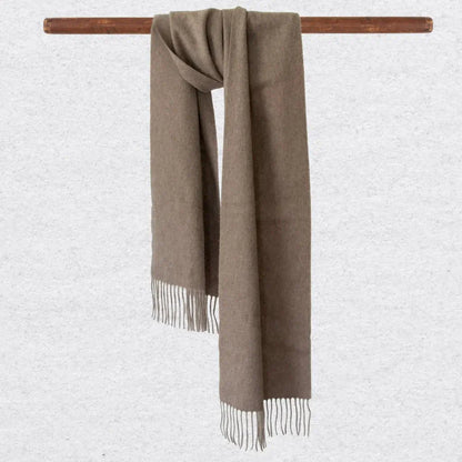 Beige scarf with fringes on a wooden rod against a light gray background