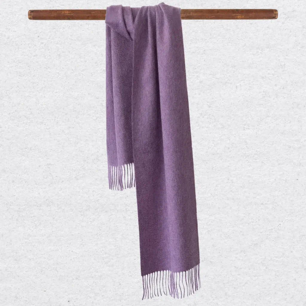 Lilac cashmere scarf with tassels on a wooden rod against a light gray background