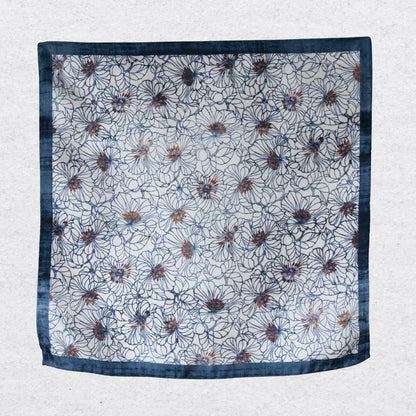 Floral patterned silk pocket square hanging against a textured grey background